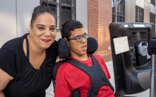 A smiling mother with her teenage son in a wheelchair on a New York sidewalk
