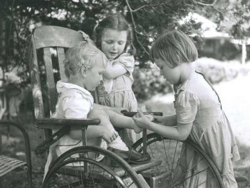 historic image of a child in a wheelchair assisted by two other children