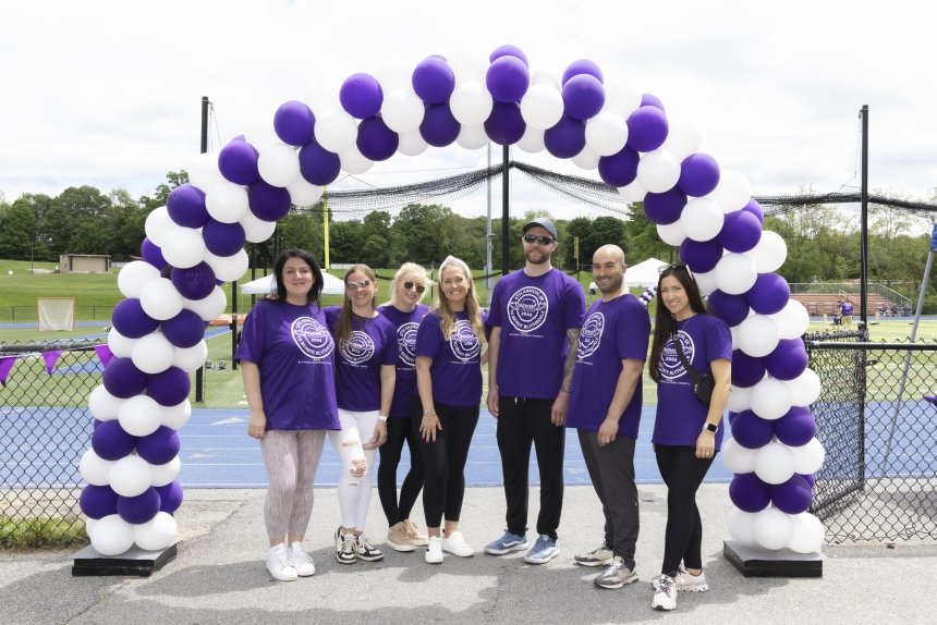 Group of people standing under a purple and white awning wearing purple